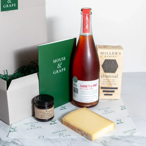 A hamper with a pink rose cider, one cheese, fruit cheese and charcoal crackers