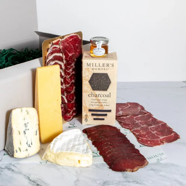 A hamper with no wine, three cheeses and three sliced, cure meats with charcoal crackers and honey